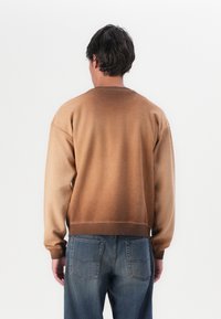Bruine gradient sweatshirt met een ronde hals en geribbelde zoom, gecombineerd met blauwe denim jeans met twee achterzakken.