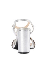 Stříbrné sandály na podpatku s nastavovacími pásky kolem kotníku, metalickým povrchem, otevřenou špičkou a černou gumovou podrážkou. Strukturovaný design vysokého blokového podpatku.
