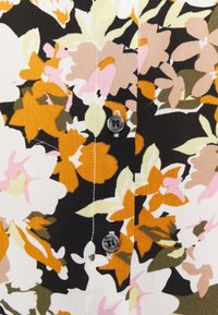 Blouse fleurie présentant un motif de fleurs blanches, roses, orange et vertes sur fond noir ; comprend des détails de boutons et des coutures visibles.