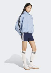 Svetlomodrá vetrovka s čiernymi pruhmi, námornícke šortky s bielymi pruhmi, biele podkolienky a biele tenisky.