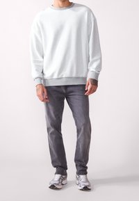 Sweat-shirt gris clair avec un col ras du cou et des poignets côtelés, associé à un jean gris foncé et des baskets argentées. Coupe décontractée, texture douce.