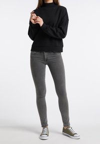 Musta, pitkähihainen collegepaita korkealla pääntiellä, yhdistetty istuviin harmaisiin farkkuihin ja vihreisiin matalavartisiin lenkkareihin, joissa on valkoiset yksityiskohdat.