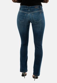 Jeans de mezclilla de lavado oscuro con un ajuste slim, ligeras marcas de desgaste y dos bolsillos traseros. Cintura estándar y acabado en el dobladillo, adecuados para un uso casual.