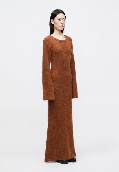 Dolga, prilegajoča obleka iz mehkega, teksturiranega rjavega pletenega blaga. Ima okroglo ovratnico in ravno silhueto do tal.