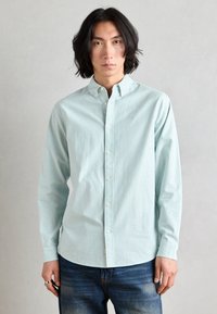 Light blue striped button-up shirt in cotton fabric with a classic collar and long sleeves, paired with dark blue denim jeans.