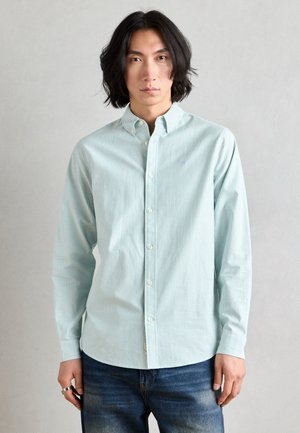 Light blue striped button-up shirt in cotton fabric with a classic collar and long sleeves, paired with dark blue denim jeans.