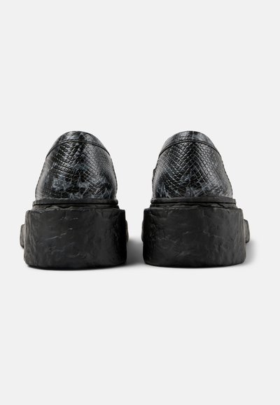 Black rubber platform shoes with snake print texture, rounded edges, and contrasting smooth black sole detail, viewed from the back.