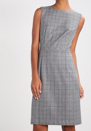 Mouwloze, knie-lange jurk met grijze ruiten en een getailleerde taille, gedragen door een persoon die tegen een effen lichte achtergrond staat.