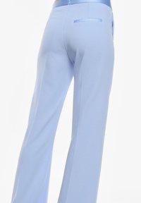 Pantaloni ampi azzurri realizzati in tessuto morbido, con chiusura a zip e una tasca sul retro con un'accenno di satin.