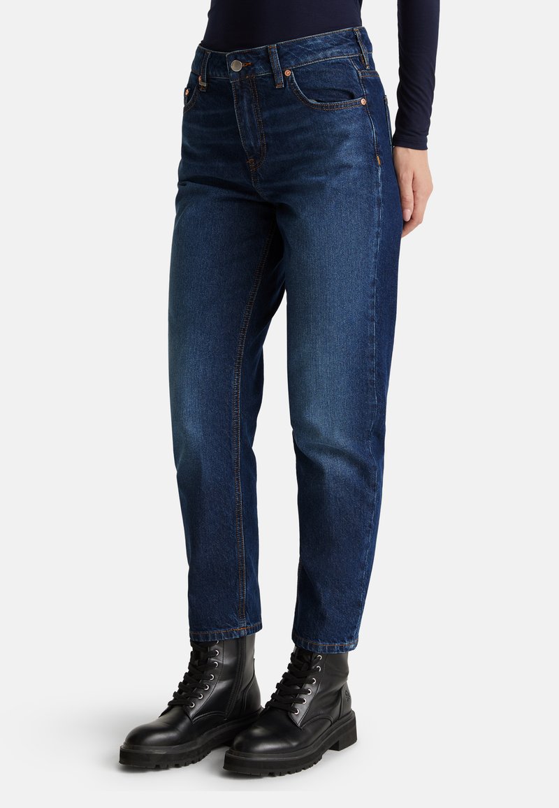 Jeans en denim bleu foncé avec une coupe droite, des détails de couture visibles et des poches avant. Associés à des bottes noires à lacets.