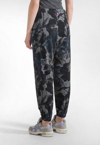 Tummansävyiset, kukkakuvioiset verkkarit, joissa löysä istuvuus, joustava vyötärönauha ja kapeat resorit. Yhdistetty harmaisiin ja vihreisiin urheilujalkineisiin.