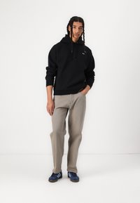 Schwarzer Hoodie mit Kapuze und Fronttasche, kombiniert mit hellgrauen, geraden Jeans. Blaue Sneaker mit drei weißen Streifen an den Seiten.