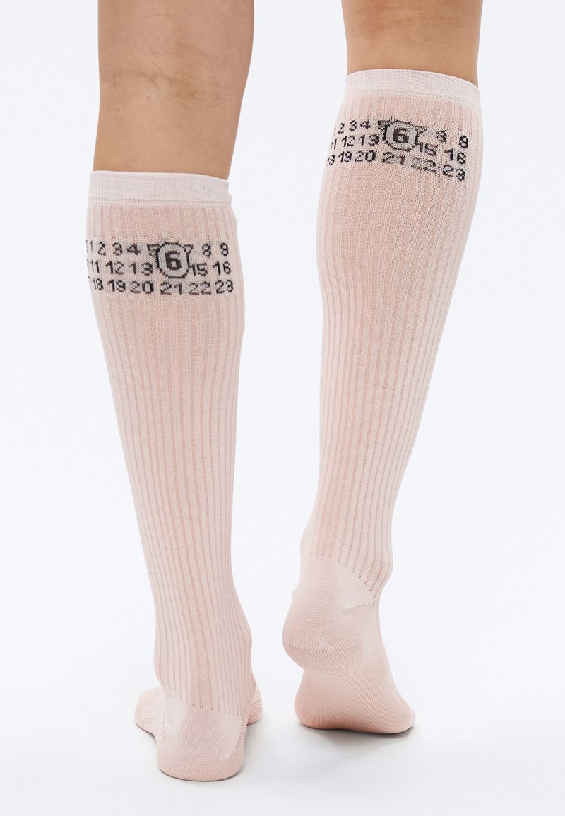 Knæhøje lyserøde sokker med ribbet tekstur, med sorte tal på bagsiden, der viser et kalenderlignende motiv. Glat materiale.