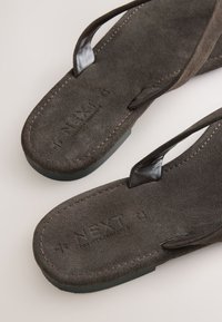 Brune ruskindsflipflops med sorte læderremme. Har tekstureret fodseng og præget logo. Syninger langs kanterne.