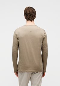 Πουκάμισο με μακριά μανίκια σε ανοιχτό μπεζ χρώμα, κατασκευασμένο από απαλό ύφασμα. Διαθέτει στρογγυλεμένο λαιμόκοψη και λεία, ελαφρώς υφασμένη επιφάνεια.