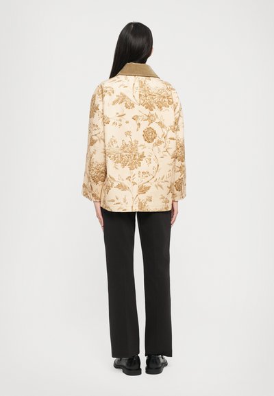 Beige takki, jossa on kukkakuosi, oliivinvihreä kaulus, löysä rakenne ja leveät hihat, yhdistetty mustiin suoriin housuihin ja kenkiin.