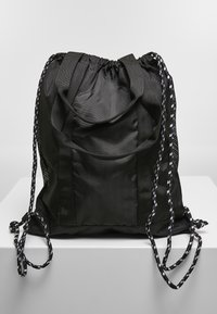 Bolsa de cuerda negra hecha de nylon texturizado, con asas duraderas, laterales de malla y correas decorativas. Diseño simple y funcional.