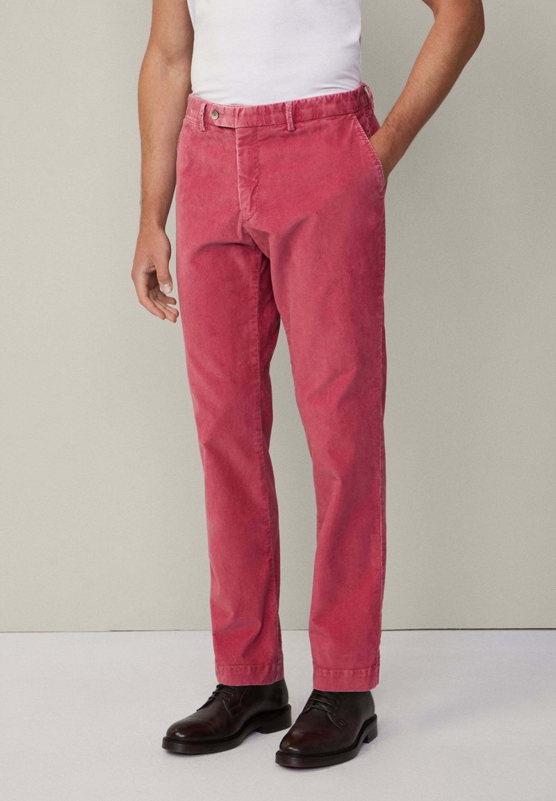 Pantalons en velours côtelé rose avec une coupe décontractée, dotés de poches avant, de passants de ceinture et d'une fermeture à bouton. Associés à des chaussures en cuir noir.