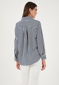 Navy and white striped button-up shirt with long sleeves, featuring a back yoke design and buttoned cuffs. Smooth fabric with a relaxed fit.
