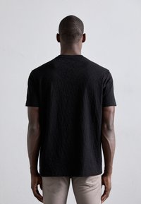 Sort kortærmet t-shirt med en tekstureret stof og et subtilt mønster. T-shirten har en rund halsudskæring og en afslappet pasform, båret med lyse bukser.