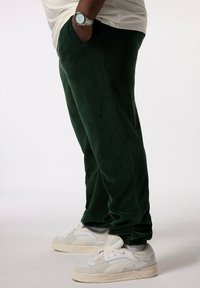 Gröna fleece-joggingbyxor med smal passform, med sidfickor och elastiska mudd, parat med vita och gråa träningsskor.