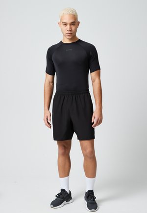 Zwart sportshirt met korte mouwen en bijpassende shorts, gemaakt van ademend materiaal. Zwarte sneakers met witte accenten en sokken maken de outfit compleet.