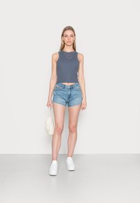 Top cropped cinza canelado, calções de ganga, ténis brancos e uma mala branca texturizada. Design simples com uma aparência casual e leve.
