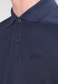 Polo bleu marine en tissu texturé, avec un col boutonné et un logo brodé discret sur la poitrine.