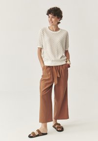Top de punto texturizado de color claro, con mangas cortas y dobladillo acanalado, combinado con pantalones de pierna ancha de color marrón claro y sandalias negras de tira.