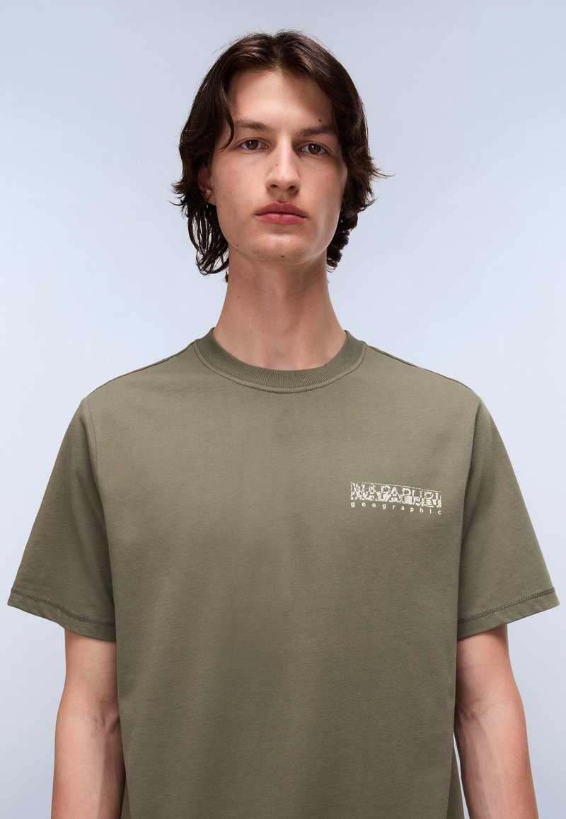 Oliwkowa koszulka z krótkim rękawem wykonana z bawełny. Posiada białe logo tekstowe na lewej piersi. Klasyczny okrągły dekolt i prosty krój.