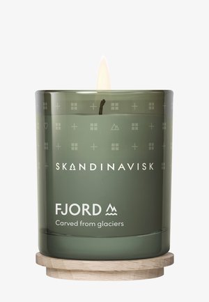 Green glass candle with a wooden base. Features minimal geometric patterns and branding, with a visible flame and wick in the center.