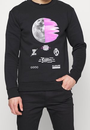 Osoba w czarnej bluzie z grafiką półksiężyca, różową smugą oraz białym tekstem z napisem "END OF DAYS" i "CLOSURE" z przodu.