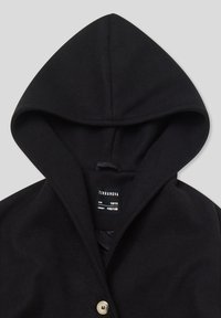 Cappotto nero con cappuccio, dotato di un unico bottone beige visibile e etichetta interna che mostra la taglia per età 12-13 anni, altezza 152-158 cm.