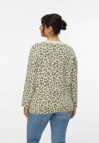 Leopardprint trui van zachte, lichtgroene stof. Heeft lange mouwen en een losse pasvorm. Gecombineerd met blauwe spijkerbroeken.
