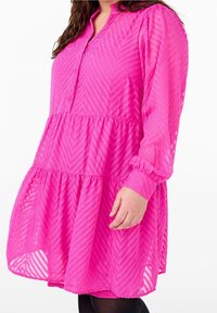 Růžové šaty ve vrstveném střihu s vzorem chevron, dlouhými rukávy, knoflíkovým výstřihem a texturovanou lehkou tkaninou.