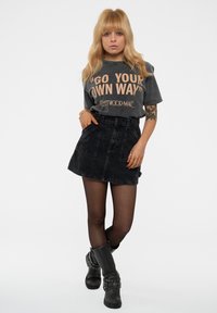 Gray graphic t-shirt with "Go Your Own Way" text, paired with a black denim mini skirt and black ankle boots with studded accents.