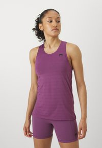 Violet sporta topiņš ar teksturētu apdari, ar melnu logotipu uz krūtīm, savienots ar atbilstošām šortiem. Gluda, pieguļoša piegriezuma dizains.