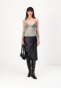 Gray denim camisole with thin straps, draped black satin skirt, black leather knee-high boots, and a small black handbag.
