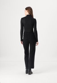 Črn dolg rokav turtleneck top, v kombinaciji z visokotopljenimi črnimi bleščečimi hlačami, viden iz ozadja, ki poudarja teksturo in prileganje tkanine.