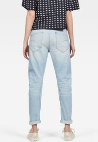 Ljust blå denim jeans med avslappnad passform, uppvikta benslut och två bakfickor med diskreta böjda sömdetaljer.