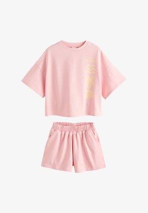 Lyserød kortærmet crop top med gule tropiske symboler, kombineret med lyserøde shorts med elastik i taljen.