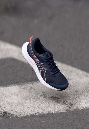 Baskets de sport navy avec tige en maille, semelle intermédiaire blanche et accents orange. Présente un bout arrondi et un design flexible et texturé.