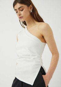 Top blanco de un solo hombro con una textura suave, un diseño ajustado y detalles fruncidos de lado, combinado con pantalones negros.