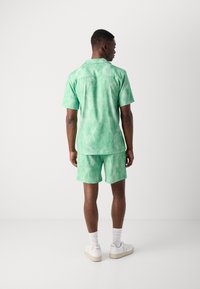 Grøn tie-dye T-shirt med korte ærmer og matchende shorts, lavet af letvægtsstof. Har en afslappet pasform og en subtil tekstur. Hvide sneakers fuldender looket.