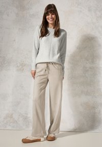 Sweat-shirt gris clair avec des poignets côtelés et un col rond, associé à un pantalon beige ample. Les chaussures ont un design texturé.
