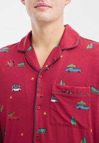 Rode pyjamablouse met groene bies, voorzien van cartoonafbeeldingen van auto's, bomen en sterren; inclusief een borstzak en knoopsluitingen.