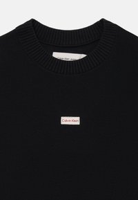 Felpa nera in cotone con scollo a girocollo e colletto a costine, caratterizzata da un piccolo patch con logo Calvin Klein bianco e rosso sul davanti.