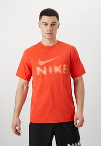 Erkki heleoranž Nike t-särgi, mis on valmistatud pehmest kangast ja mille esipoolses osas on suur, heledabež logo ja tekstikujundus. Lühikesed varrukad.
