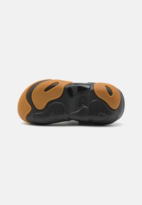 Svart idrottssko sula med ett mönstrat mönster, accentuerad med orange gummisektioner och en strömlinjeformad, funktionell design.