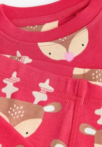 Tissu en coton rouge avec des motifs de cerfs et des accents marron clair et crème. Encolure ronde avec des coutures lisses et un design ludique.